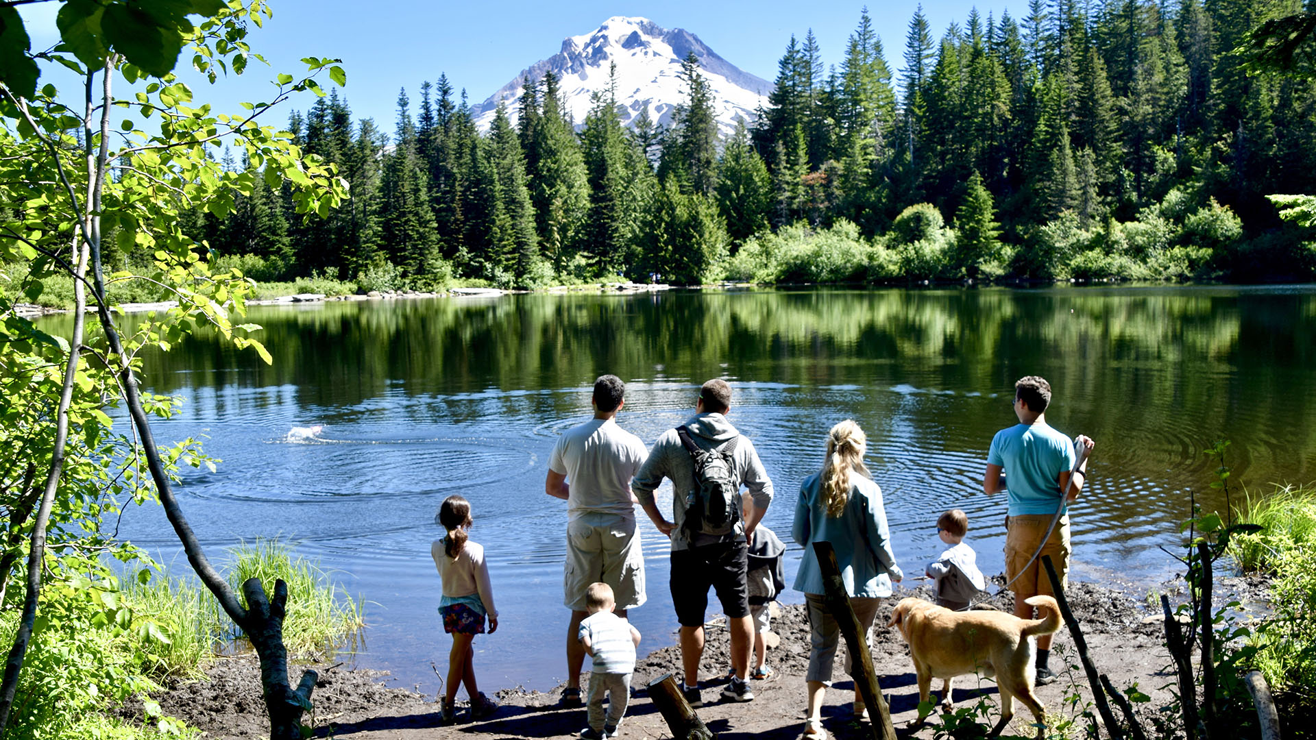 Une famille fait sauter des pierres dans le lac Mirror, perturbant le reflet du mont Hood.