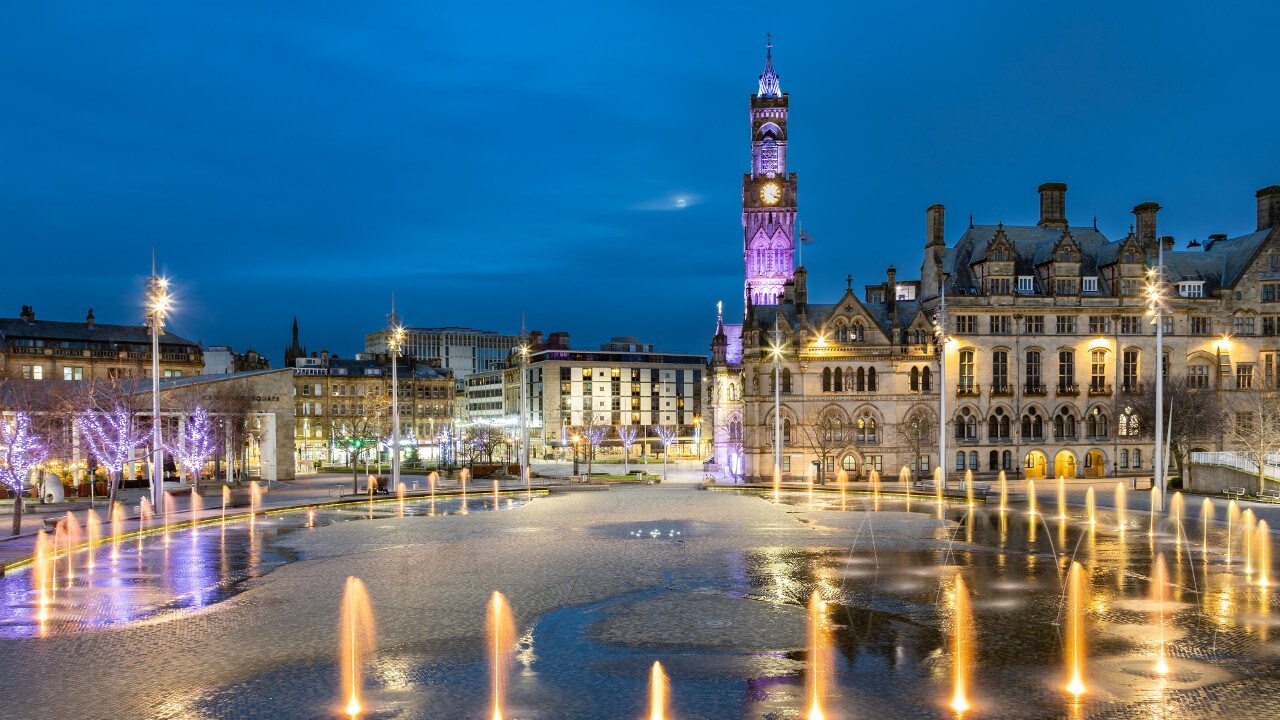 Dramatic night shot of Bradford City Hall reflected in the mirror pool in the city park.