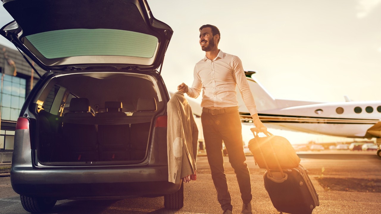 Happy businessman going on a business travel but first he has to pack his stuff into the car.